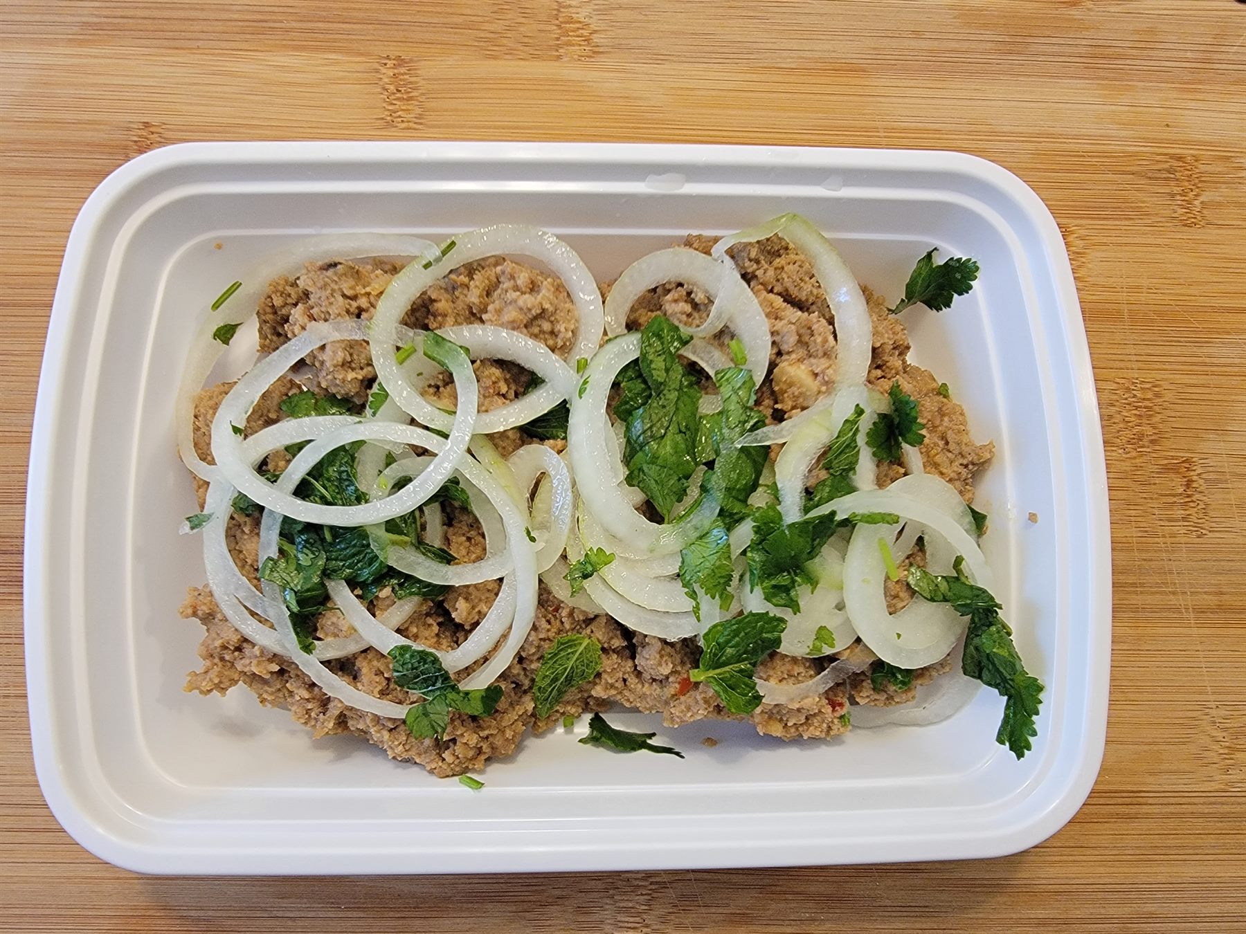 BBQ meat with onions and herbs in a takeout tray